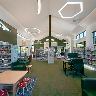 The interior of a small library, containing green carpeted floors and walls, bright white ceilings and bookshelves around the sides.