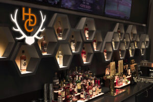 A series of hexagonal shelves house liquor bottles as the backdrop of a bar.