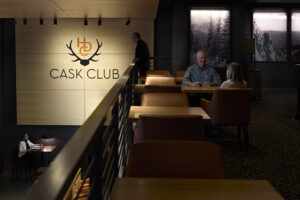 A row of booth-style seats along a railing. A man in the background stands at the railing and looks over the lower level of the lounge below.