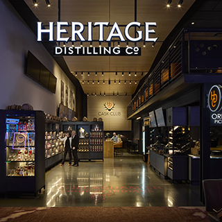 The entry to a dimly lit tasting room space. A sign over the entry reads, "Heritage Distilling Co."