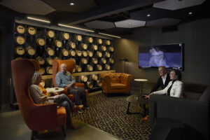 A lounge seating area with several people in high-backed chairs in front of a wall of casks.