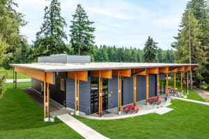 A single-story rectangular building with dark walls and large wooden overhangs. It is built into a hillside that slopes down gently away from the viewer.