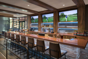 A warmly lit wooden bar has several TVs in the background.