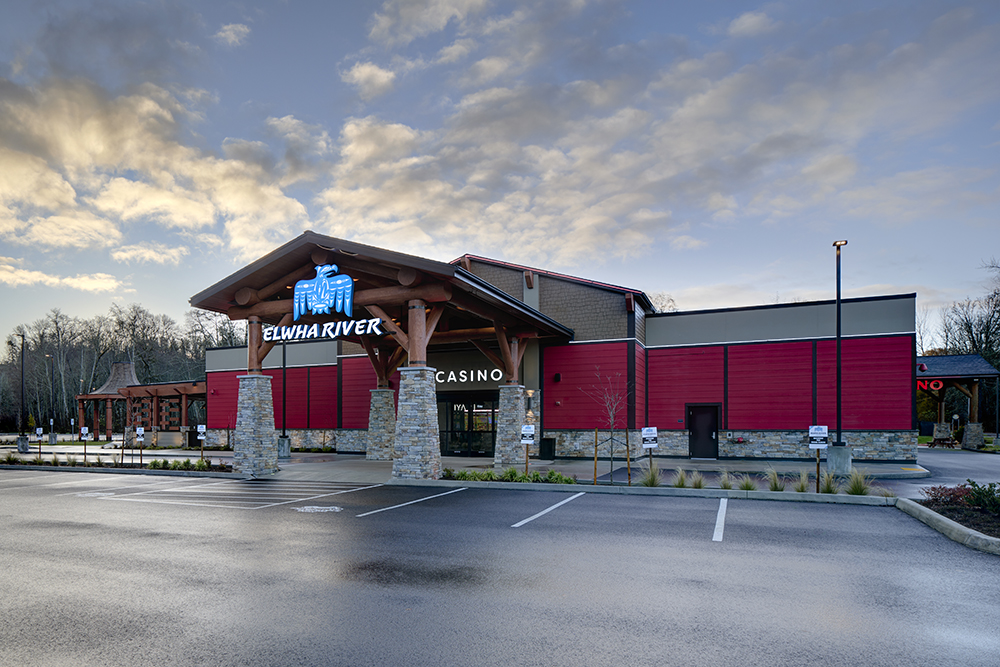The exterior of the Elwha River Casino, a red-walled building with a large covered entryway made of round wood logs and river rock columns.