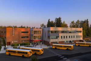 Four school busses are lined up outside a large three-story junior high school building.