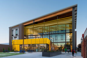 A dramatic black and yellow building juts upward at a slight angle. A large overhang shades the window wall at the front. A smaller entry way is banded with yellow above it.