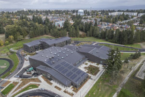 An aerial view of Evergreen High School, made up of several very large dark-colored buildings. Areas of the roof are topped with solar panels and the two buildings are connected by a sky bridge.