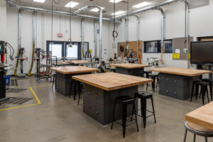 Several black tables with wooden countertops are arranged within a school shop.
