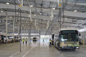 A bus is being charged from cables hanging from the roof of a large garage building.