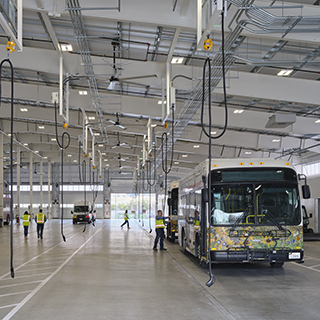 A bus is being charged from cables hanging from the roof of a large garage building.