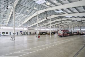 Several busses and transit vehicles are parked inside a very large white-painted garage building.
