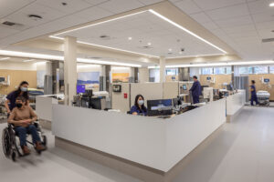 Nurses work at a central station surrounded by patient rooms that are partitioned by privacy curtains.