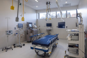 An empty procedural room contains a blue exam gurney and various medical equipment.