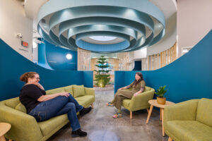 Two people sit in green chairs underneath a large circular ceiling fixture.