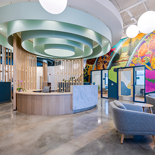A lobby with a central wooden reception desk has a large circular fixture overhead. A colorful mural decorates the far wall.