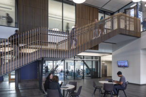 College students walk up a large floating staircase with vertical wood railings.