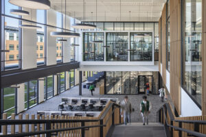 College students walk up the stairs in a large two-story atrium with floor-to-ceiling windows.