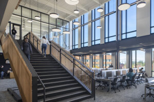 College students walk up the stairs in a large two-story atrium with floor-to-ceiling windows.
