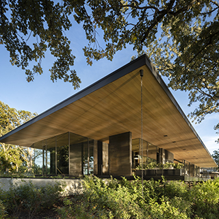 A broad wood roof cantilevers over glass and concrete walls.