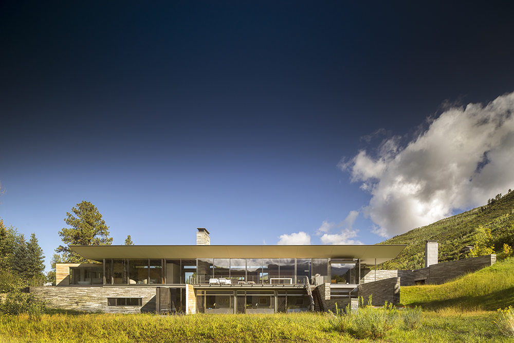 Independence-Pass-Residence-Gallery A two-story house with a wide overhanging roof sits in a meadow with a blue sky overhead.