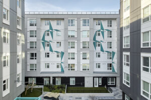 The outside wall of a tall apartment building. It is mostly light gray with geometrical teal designs.