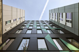 The side of a large apartment building with many rectangular windows and a gray and teal facade.