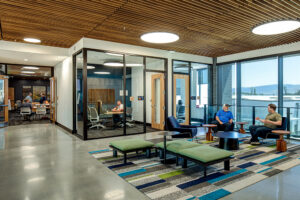 An open lobby with a wood ceiling and several glass-walled conference rooms in the background. Several groups of people are sitting around having conversations.
