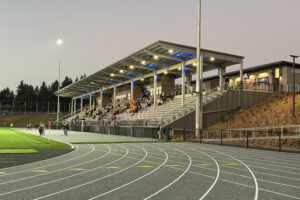 A metal stadium lit up with blue and green lights under the roof at the side of a running track.