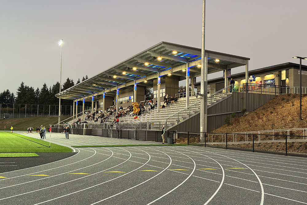 A metal stadium lit up with blue and green lights under the roof at the side of a running track.