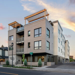 A three-story gray apartment building has large windows and wood pergolas on top of the roof.