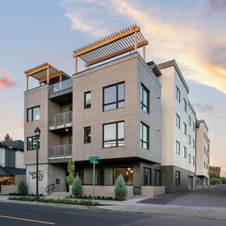 A three-story gray apartment building has large windows and wood pergolas on top of the roof.