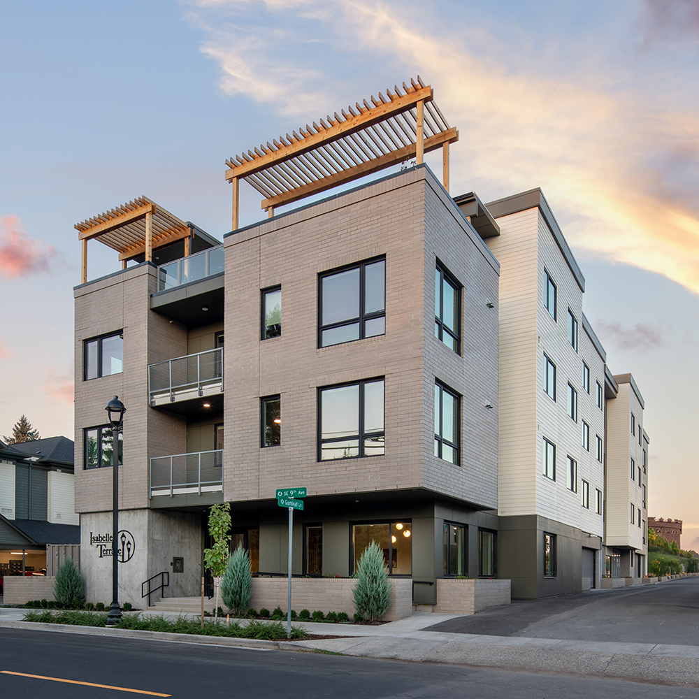 A three-story gray apartment building has large windows and wood pergolas on top of the roof.