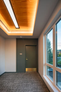 An apartment building hallway ends in a dark green door. A wood ceiling is warmly lit overhead.