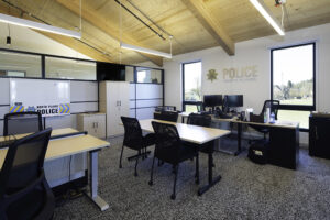 Several rows of desks are arranged in a room with a wood ceiling. The back wall has a sign reading "POLICE".